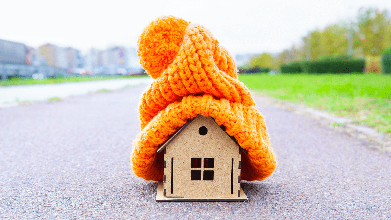 Cozy winter home concept with a knitted hat on a wooden house model (winter saving tips blog)